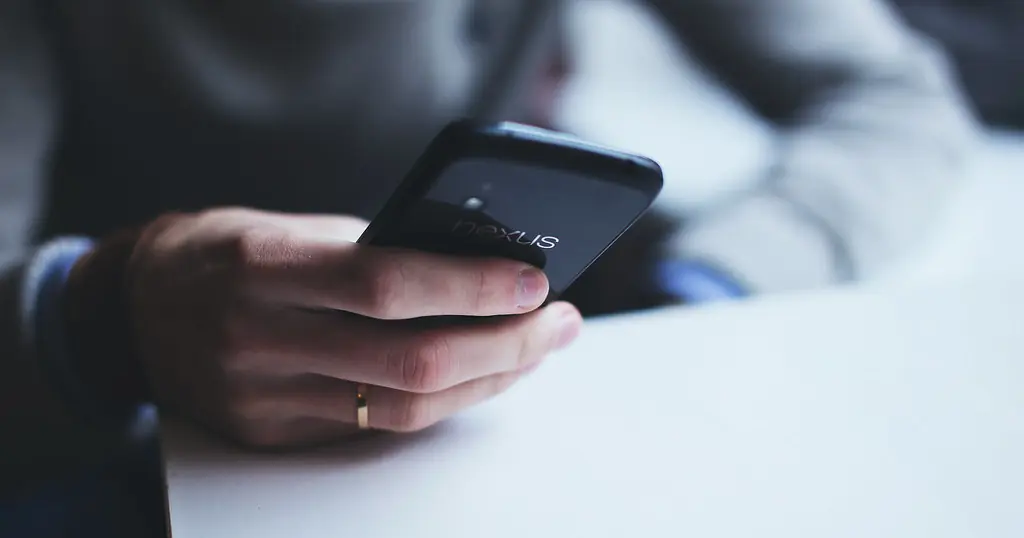 En hånd holder en mobil over et hvidt bord, klar til at skrive en god datingprofil