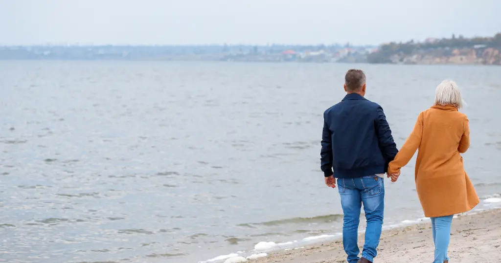 Dating sider senior: et ældre par går hånd i hånd langs stranden